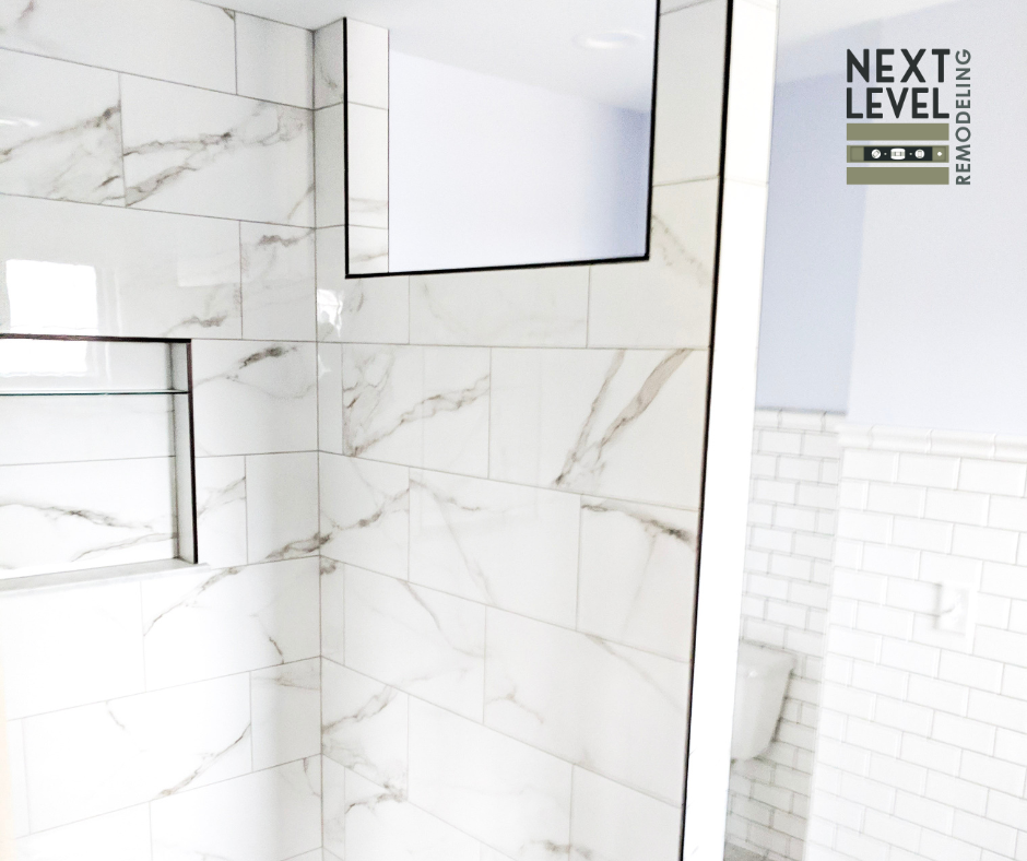 Modern bathroom remodeling with large-format marble-look shower tiles, recessed shower niche, frameless mirror cabinet, and contemporary finishes by Next Level Remodeling MN.