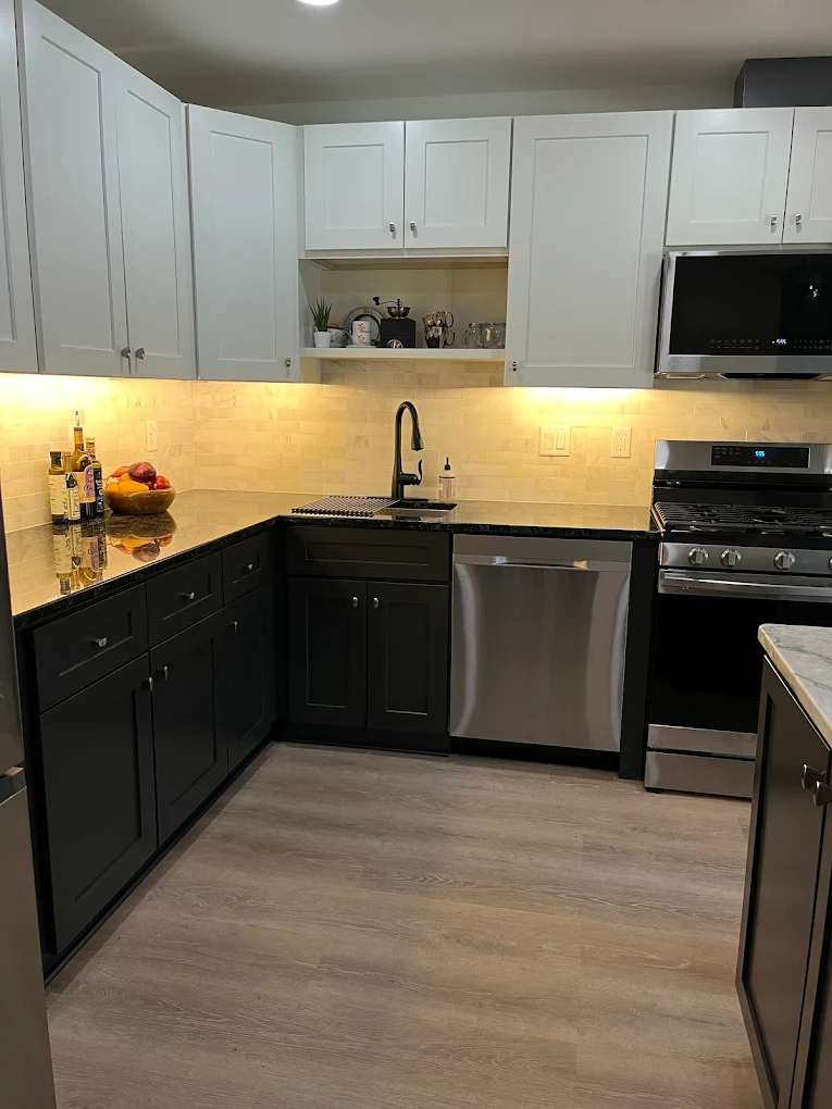 Modern kitchen remodeling with white upper cabinets, black lower cabinets, granite countertops, stainless steel appliances, subway tile backsplash, and under-cabinet lighting by Next Level Remodeling MN.