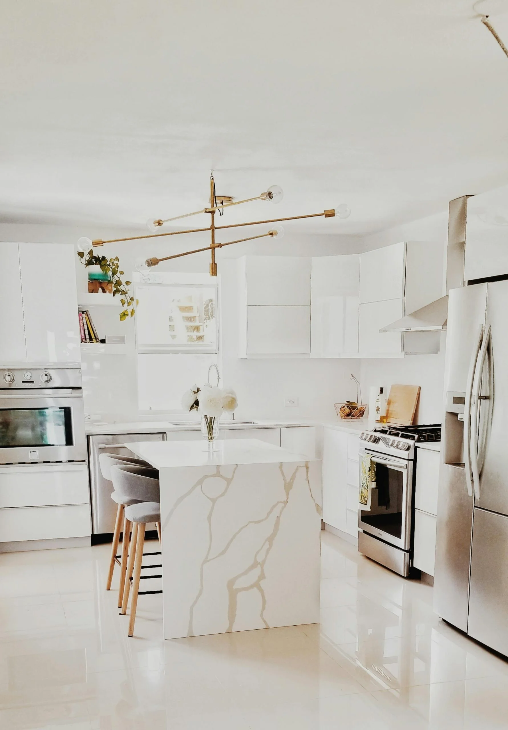 Modern white kitchen remodeling with quartz waterfall island, stainless steel appliances, custom cabinetry, and pendant lighting by Next Level Remodeling MN.