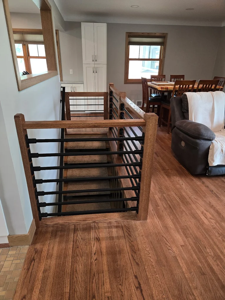 Remodeled staircase with custom wood posts, black horizontal metal railings, hardwood flooring, and modern interior finishes by Next Level Remodeling MN.